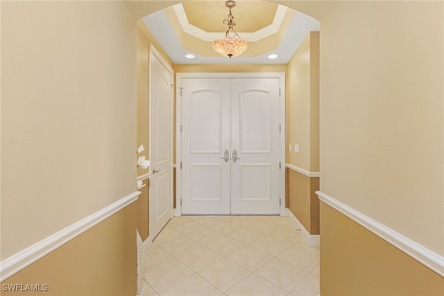 hall featuring a tray ceiling, light tile patterned floors, baseboards, and arched walkways