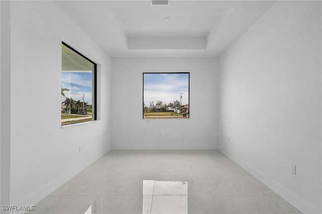 empty room featuring a raised ceiling, a healthy amount of sunlight, baseboards, and visible vents