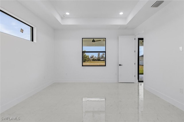 spare room with a tray ceiling, visible vents, baseboards, and a healthy amount of sunlight