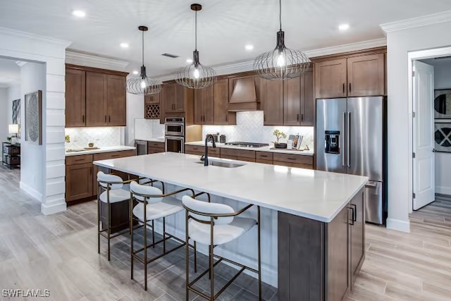 kitchen with ornamental molding, custom range hood, a sink, appliances with stainless steel finishes, and light countertops