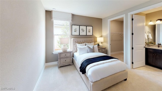 bedroom featuring baseboards, a closet, ensuite bathroom, light carpet, and a walk in closet