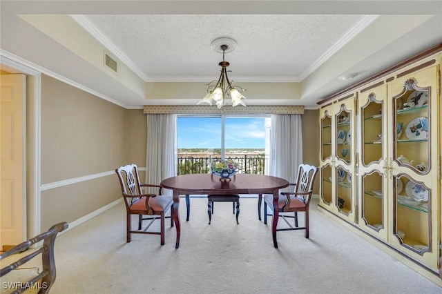 carpeted dining room featuring a textured ceiling, a raised ceiling, ornamental molding, and a chandelier