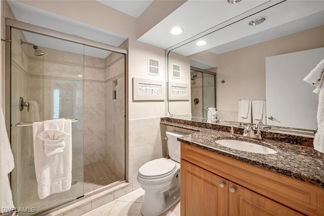 bathroom with tile walls, toilet, a stall shower, tile patterned floors, and vanity