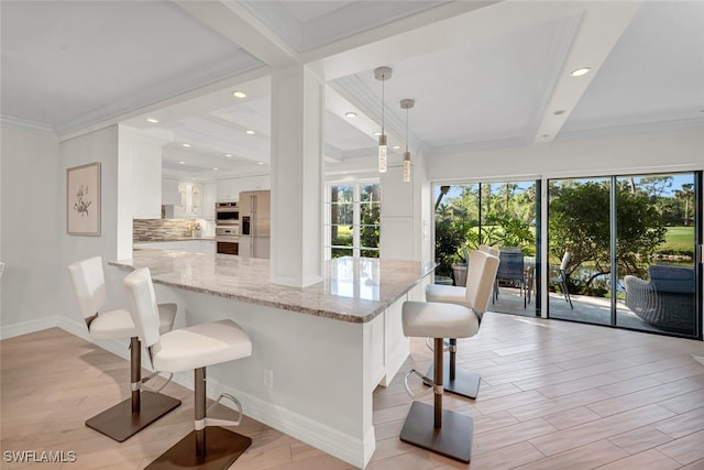 kitchen featuring tasteful backsplash, a kitchen bar, light stone counters, a peninsula, and white cabinetry