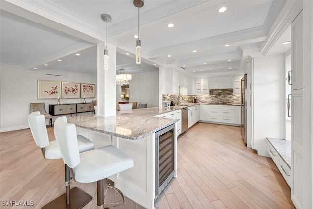 kitchen featuring beverage cooler, a peninsula, ornamental molding, white cabinets, and appliances with stainless steel finishes