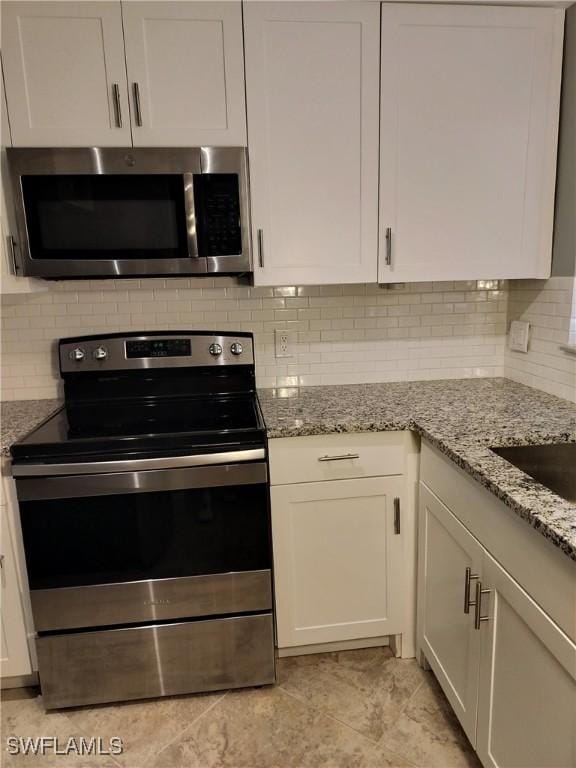 kitchen with decorative backsplash, appliances with stainless steel finishes, white cabinetry, and light stone countertops