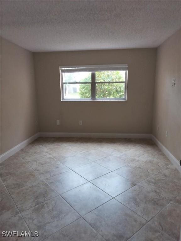 empty room featuring light tile patterned floors, baseboards, and a textured ceiling