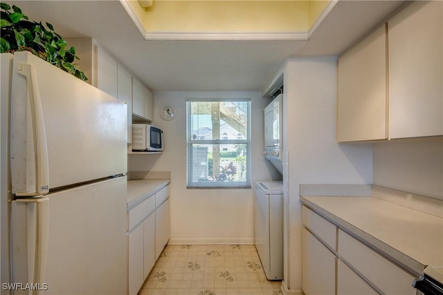 kitchen with white appliances, light floors, light countertops, stacked washer and dryer, and white cabinetry