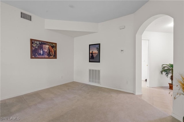 unfurnished room with arched walkways, visible vents, and light carpet