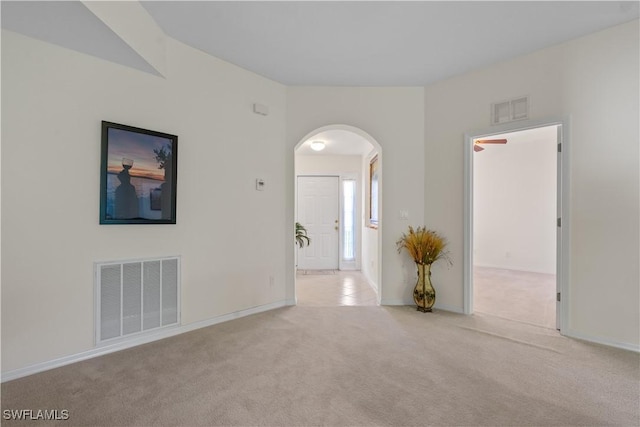 empty room featuring baseboards, light colored carpet, visible vents, and arched walkways