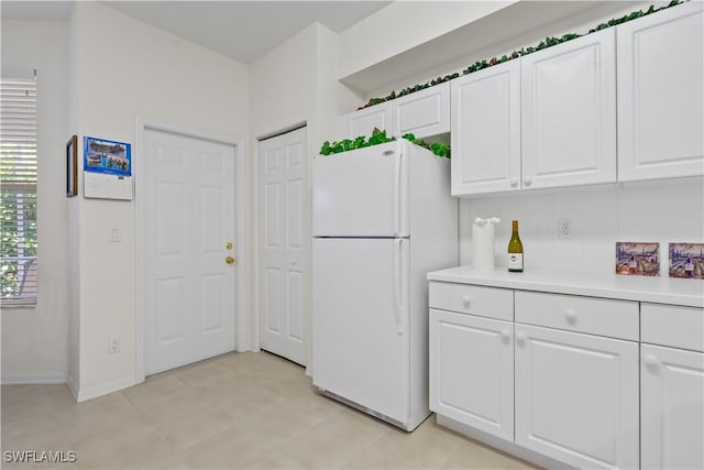 kitchen with white cabinets, light countertops, freestanding refrigerator, and baseboards