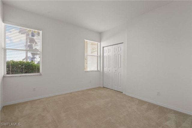 unfurnished bedroom with light carpet, multiple windows, a closet, and baseboards