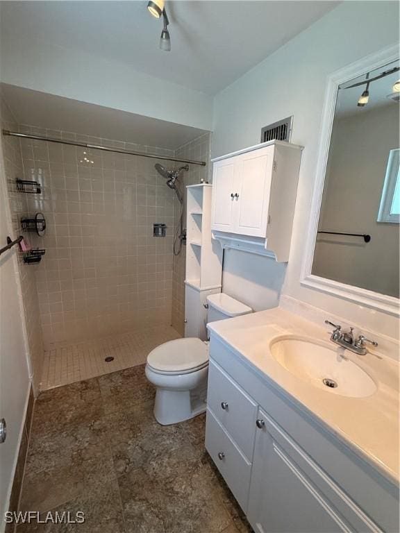 bathroom featuring visible vents, toilet, vanity, and a tile shower