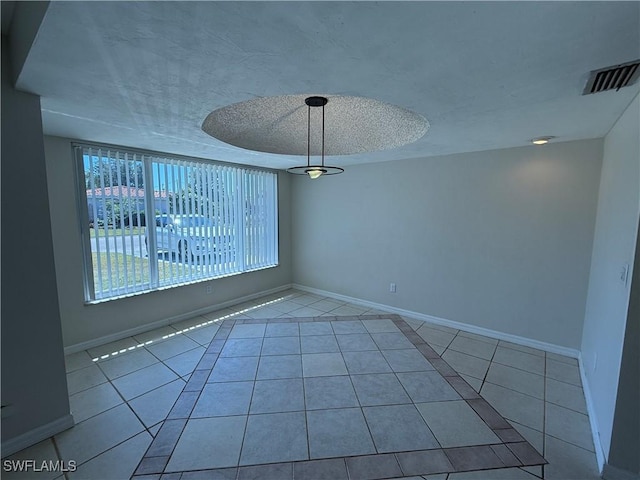 tiled spare room with visible vents, a textured ceiling, and baseboards