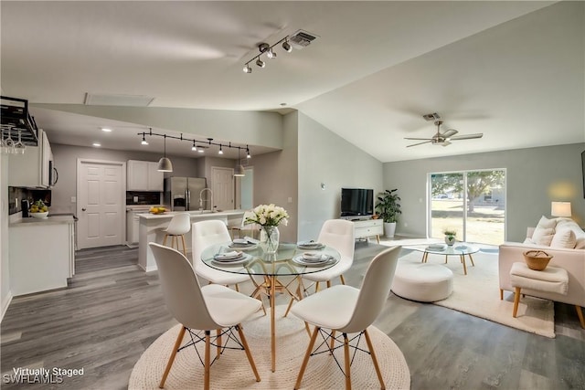 dining area with a ceiling fan, vaulted ceiling, wood finished floors, and visible vents