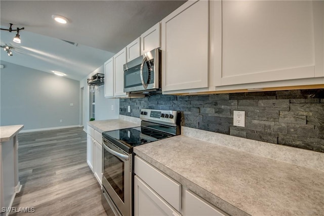 kitchen with stainless steel appliances, light countertops, vaulted ceiling, white cabinetry, and backsplash