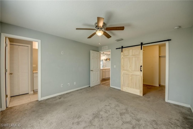 unfurnished bedroom featuring a barn door, carpet floors, visible vents, and a walk in closet