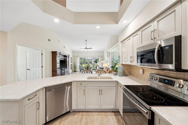 kitchen featuring decorative backsplash, a peninsula, light wood-style floors, stainless steel appliances, and a sink