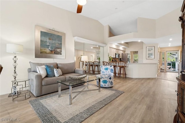 living area featuring a ceiling fan, light wood-style floors, and high vaulted ceiling