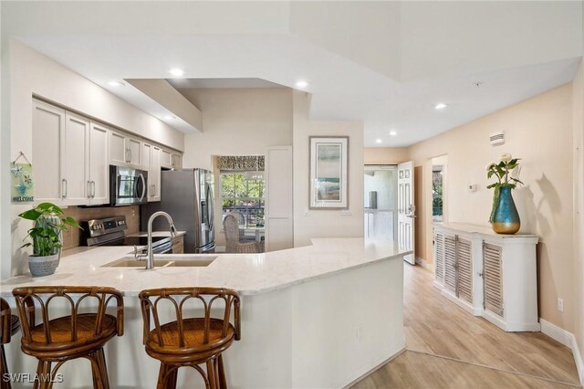 kitchen featuring light stone countertops, a peninsula, appliances with stainless steel finishes, a kitchen bar, and light wood-type flooring