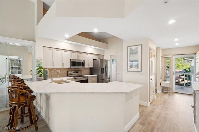 kitchen with a peninsula, light wood-style flooring, a sink, appliances with stainless steel finishes, and tasteful backsplash