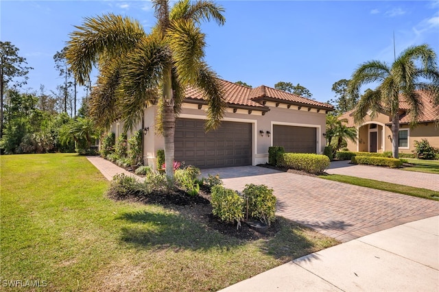 mediterranean / spanish-style home featuring a front lawn, a tiled roof, stucco siding, decorative driveway, and a garage