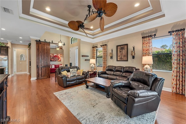 living room with a ceiling fan, visible vents, a barn door, light wood-style floors, and a raised ceiling