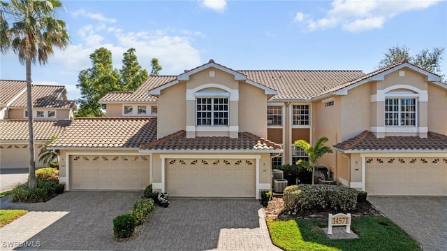 mediterranean / spanish home with a tiled roof, decorative driveway, a garage, and stucco siding