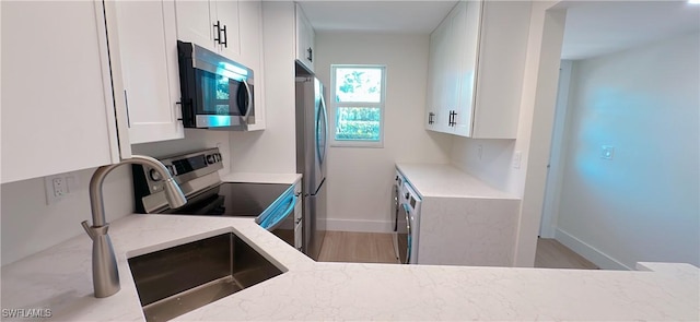 kitchen featuring a sink, appliances with stainless steel finishes, white cabinetry, and light stone countertops