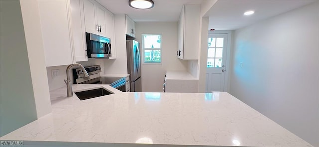 kitchen with a sink, white cabinets, stainless steel appliances, and light stone countertops