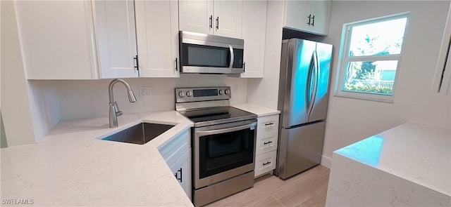 kitchen with white cabinetry, light stone countertops, appliances with stainless steel finishes, and a sink