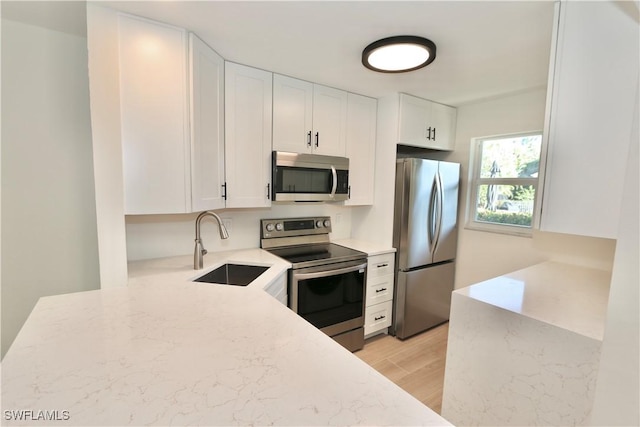 kitchen featuring light stone counters, light wood-style flooring, stainless steel appliances, white cabinetry, and a sink