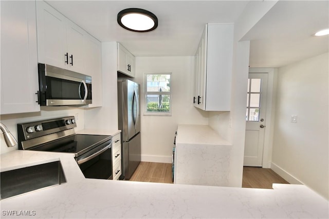 kitchen with white cabinetry, light wood finished floors, baseboards, and appliances with stainless steel finishes