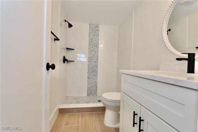 full bathroom featuring a tile shower, toilet, and vanity