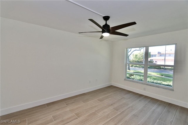 empty room with light wood finished floors, a ceiling fan, and baseboards