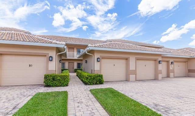 townhome / multi-family property featuring stucco siding, an attached garage, decorative driveway, and a balcony