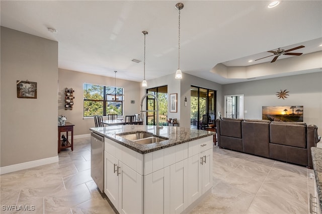 kitchen featuring an island with sink, a sink, stainless steel dishwasher, dark stone counters, and baseboards