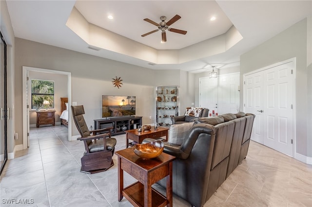 living room with visible vents, a raised ceiling, baseboards, and ceiling fan