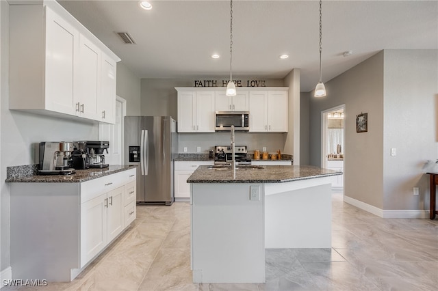 kitchen with an island with sink, dark stone countertops, a sink, white cabinetry, and appliances with stainless steel finishes