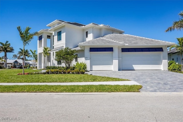 prairie-style house with a front lawn, decorative driveway, a garage, and stucco siding