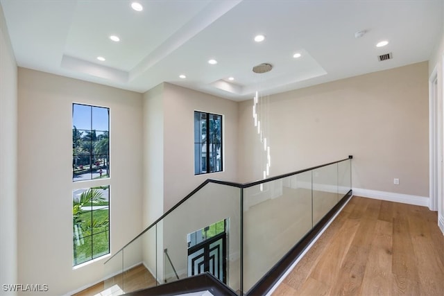 hallway with a raised ceiling, an upstairs landing, and a healthy amount of sunlight