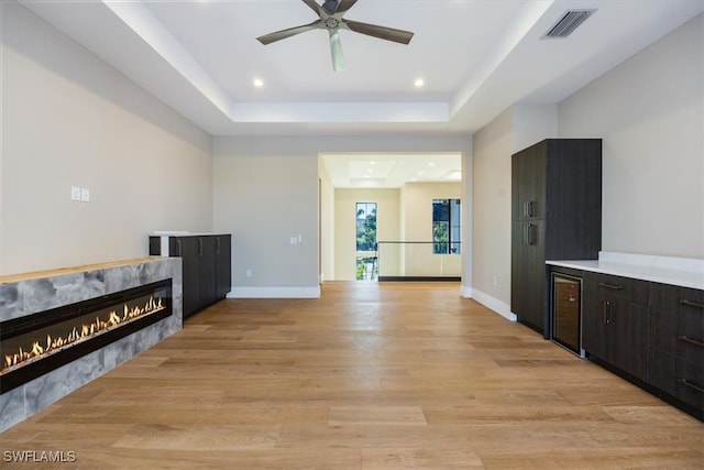 living area featuring visible vents, baseboards, a tray ceiling, a fireplace, and light wood-style floors