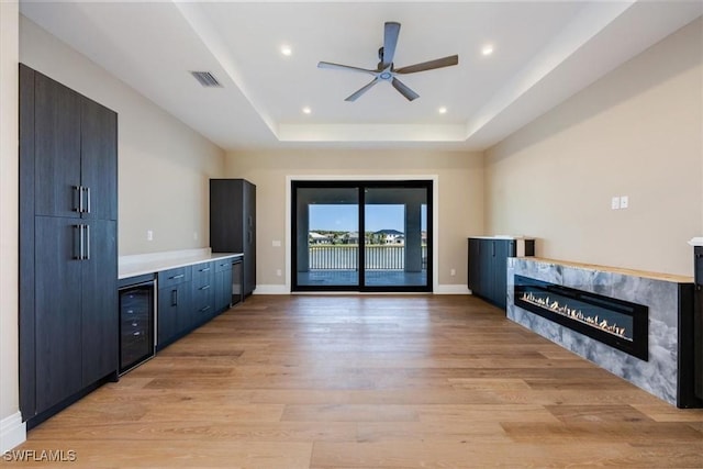 interior space featuring visible vents, beverage cooler, a premium fireplace, light wood-style floors, and a raised ceiling