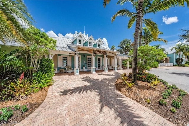 rear view of house featuring a standing seam roof, a porch, decorative driveway, and metal roof