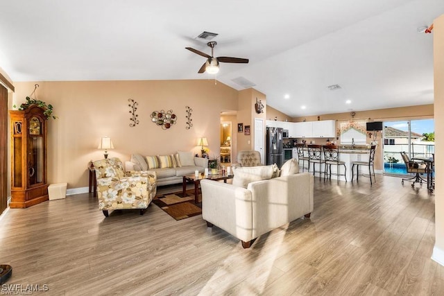 living area with visible vents, ceiling fan, vaulted ceiling, and light wood-style floors