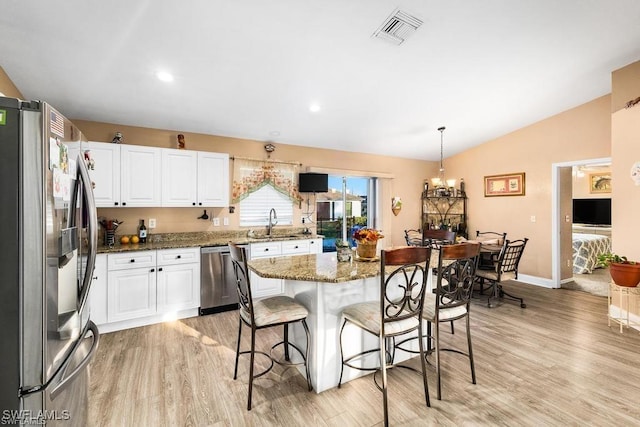 kitchen featuring visible vents, a kitchen bar, lofted ceiling, appliances with stainless steel finishes, and a sink