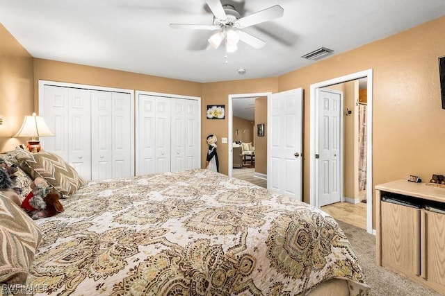 bedroom featuring a ceiling fan, visible vents, multiple closets, and light carpet