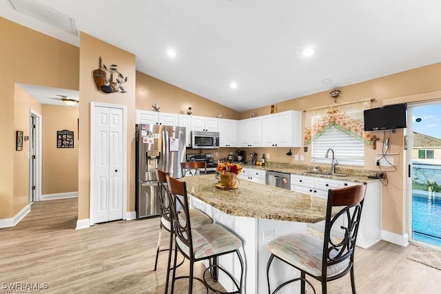 kitchen with a breakfast bar, a sink, vaulted ceiling, appliances with stainless steel finishes, and white cabinetry