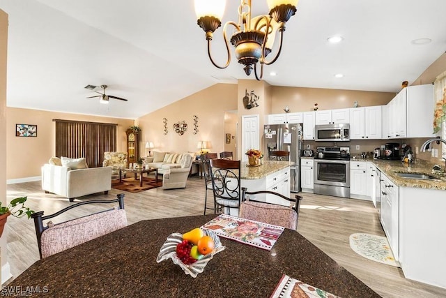 kitchen with open floor plan, light wood-type flooring, lofted ceiling, appliances with stainless steel finishes, and a sink