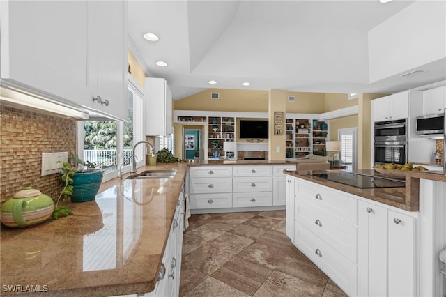 kitchen with a sink, dark stone countertops, stainless steel appliances, a peninsula, and white cabinets